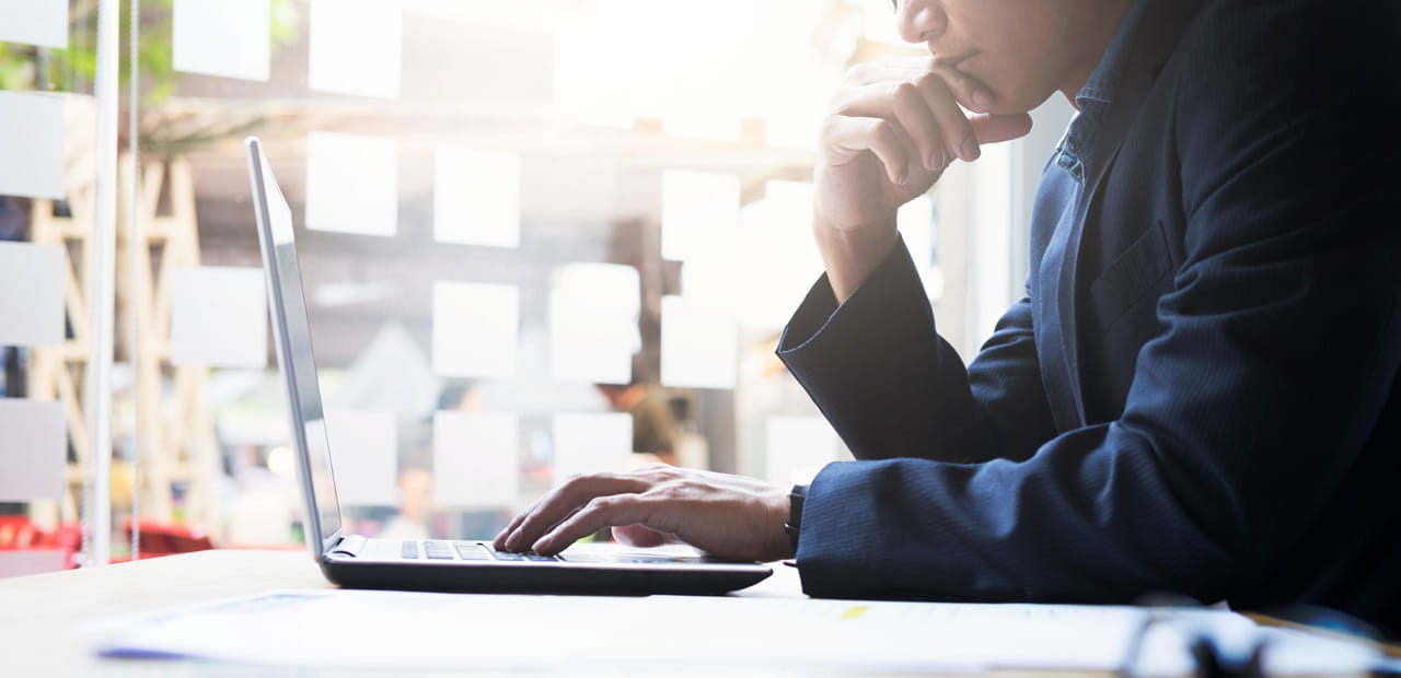 Seated man reading his laptop computer.