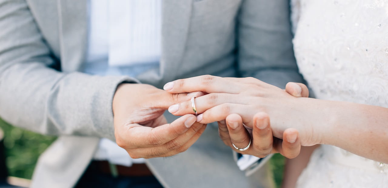 Groom putting ring on bride's finger during marriage ceremony.