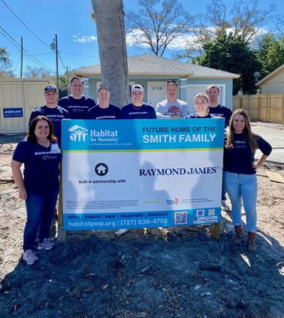 Raymond James volunteer pose by Habitat sign that says 